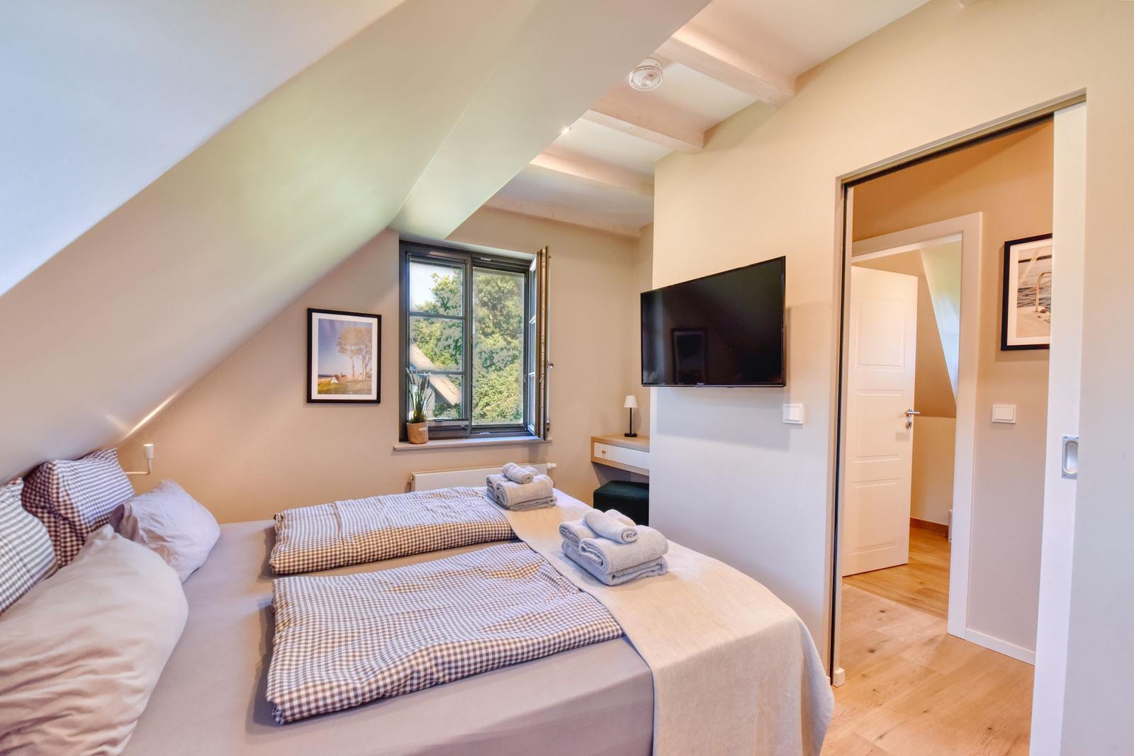 Bedroom with sloped ceiling, bed, window, TV, and adjacent door.