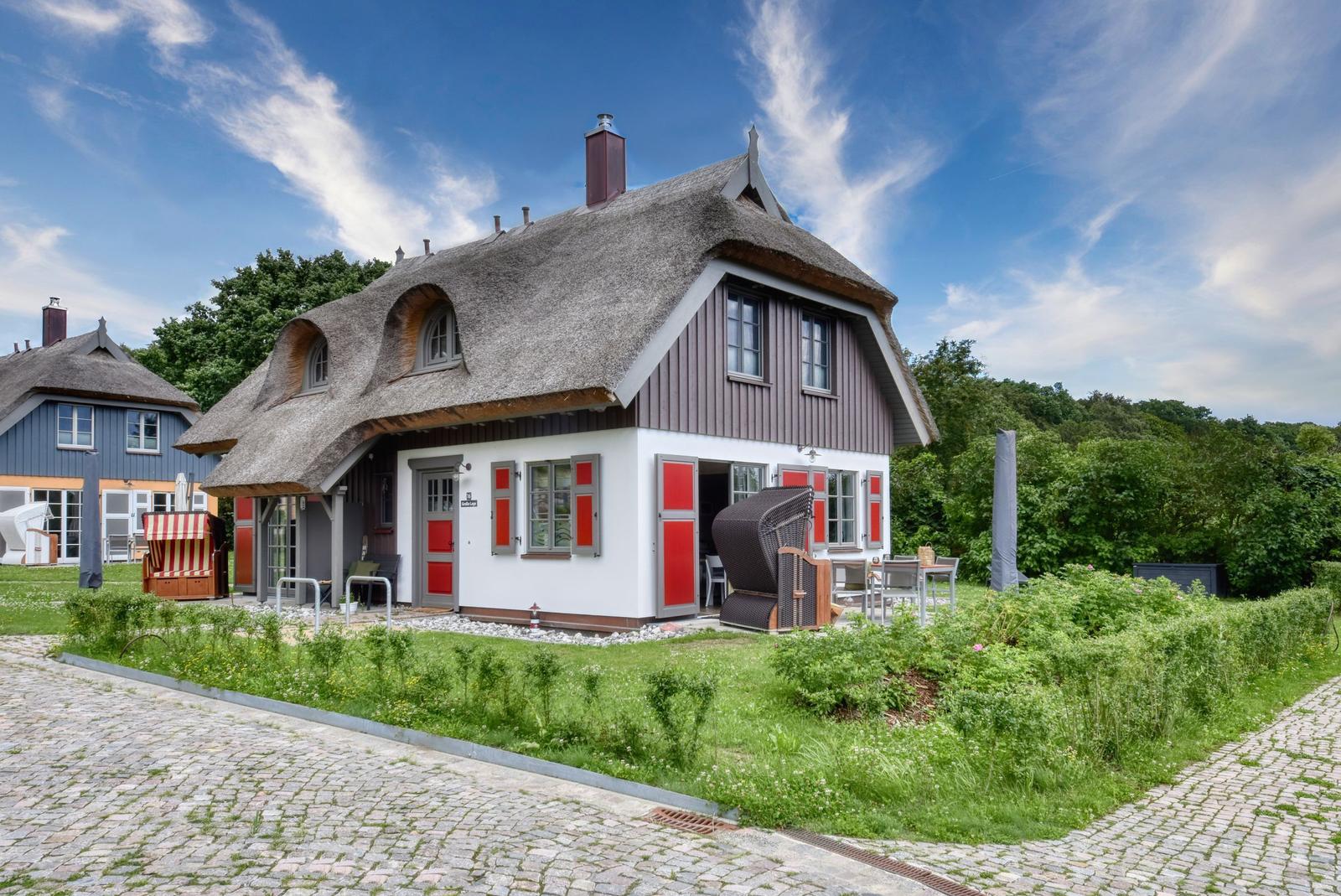 House with thatched roof, red shutters, and garden area.