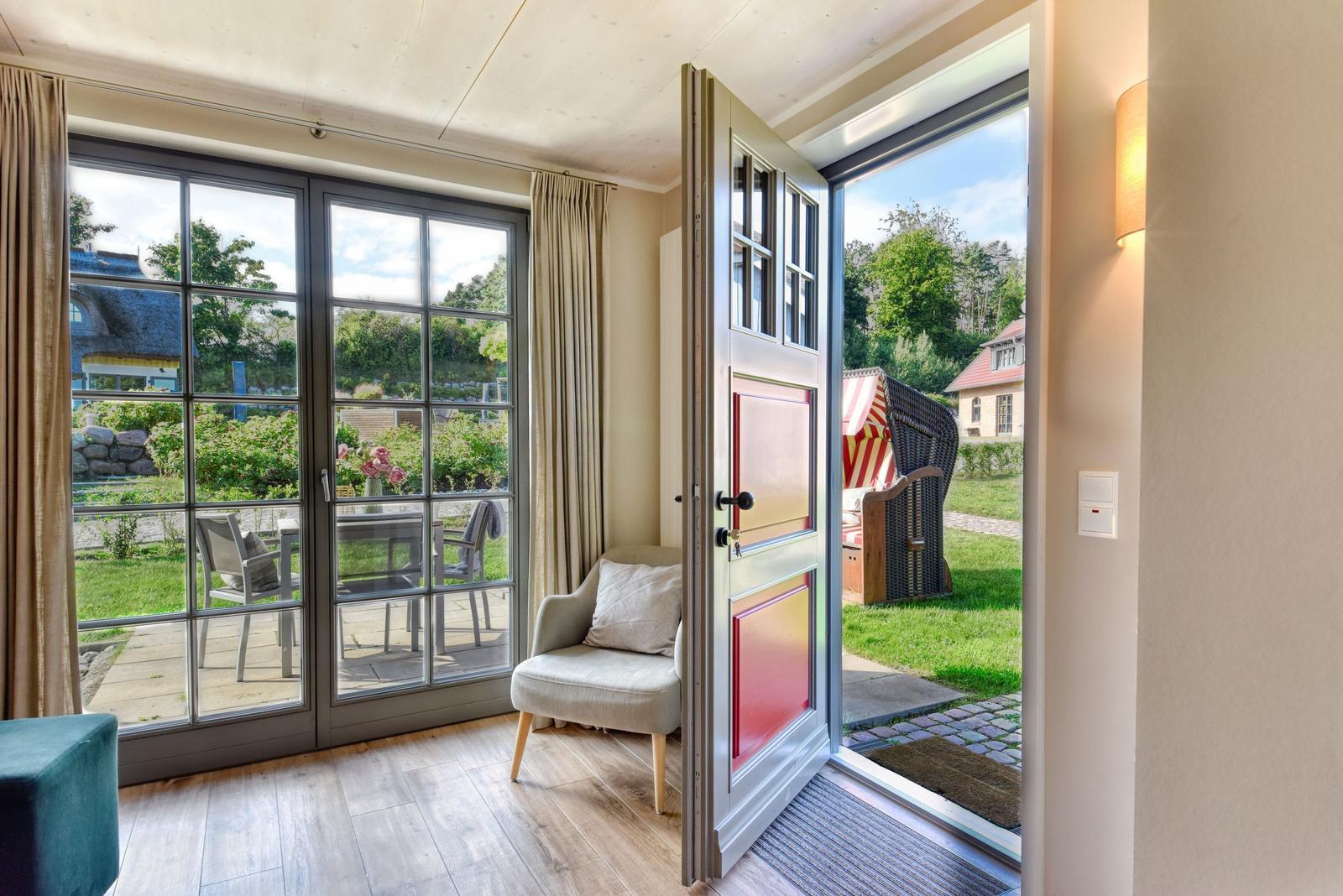 House with large window and door to garden. Seating area and view of green space.