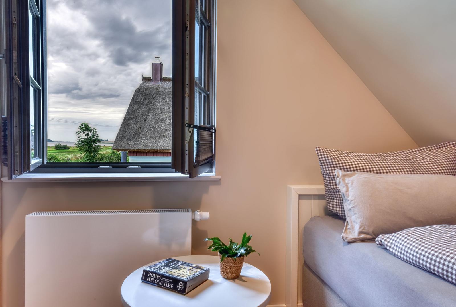 Schlafzimmer mit Blick auf Dachhütte und Landschaft. Bett, Nachttisch und Heizung sichtbar.