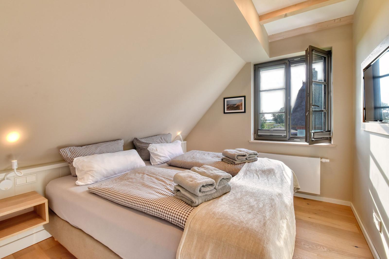 Schlafzimmer mit Doppelbett, Fenster und TV. Holzboden und schräge Decke.
