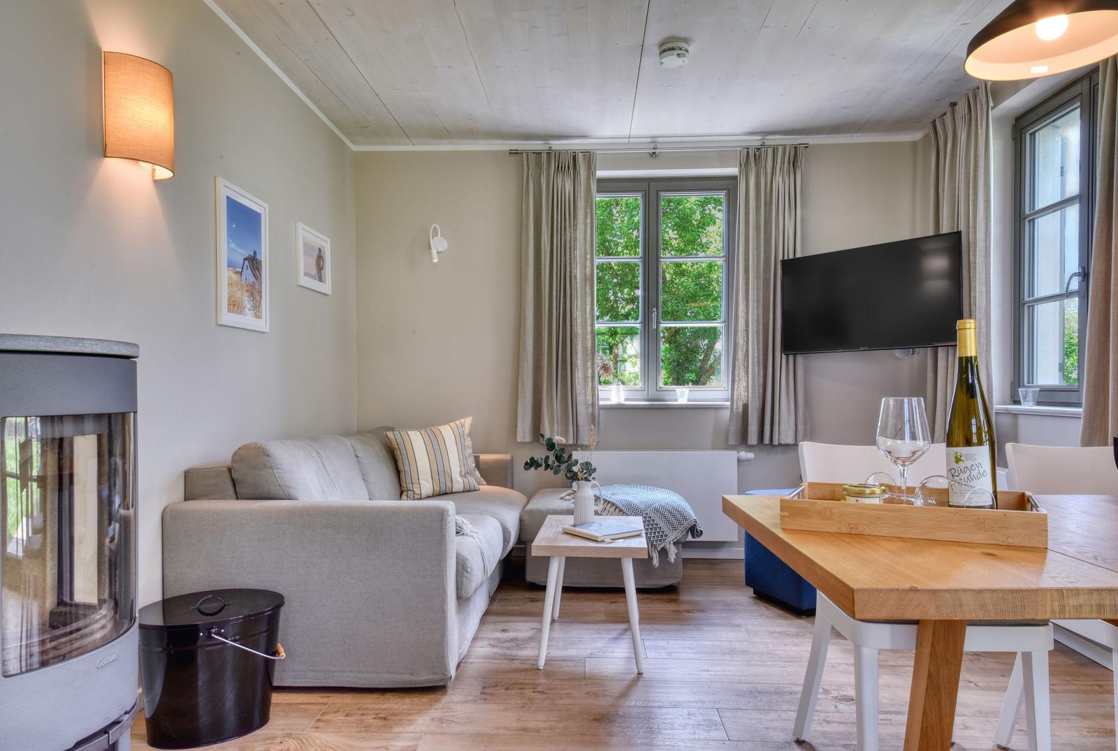 Wohn- und Essbereich mit Sofa, Fernseher und Holztisch. Fenster mit Blick auf Bäume.