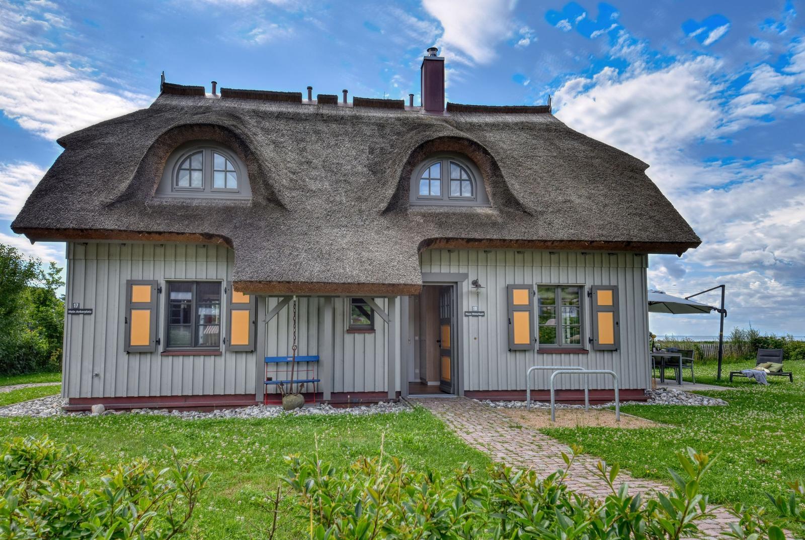 Haus mit Strohdach, gelben Fensterläden und Terrasse mit Sonnenschirm.