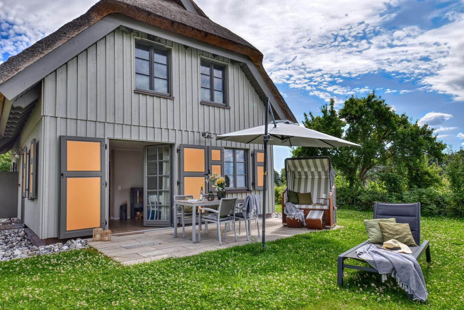 Haus mit Dachstuhl, Terrasse, Tisch, Stühle, Sonnenschirm und Liege im Garten.