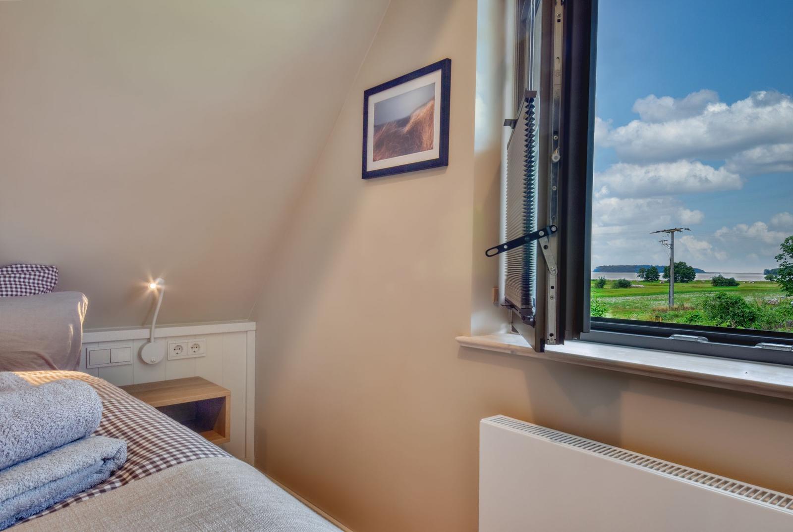 Schlafzimmer mit Blick auf Feld und Himmel. Bett, Nachttisch und Heizung sind sichtbar.