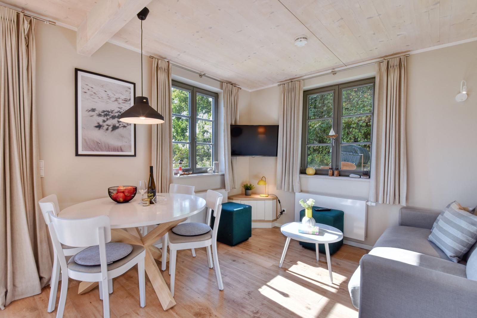 Wohn- und Essbereich mit Tisch, Stühlen, Sofa und Fenstern. Decke mit Holzbalken.
