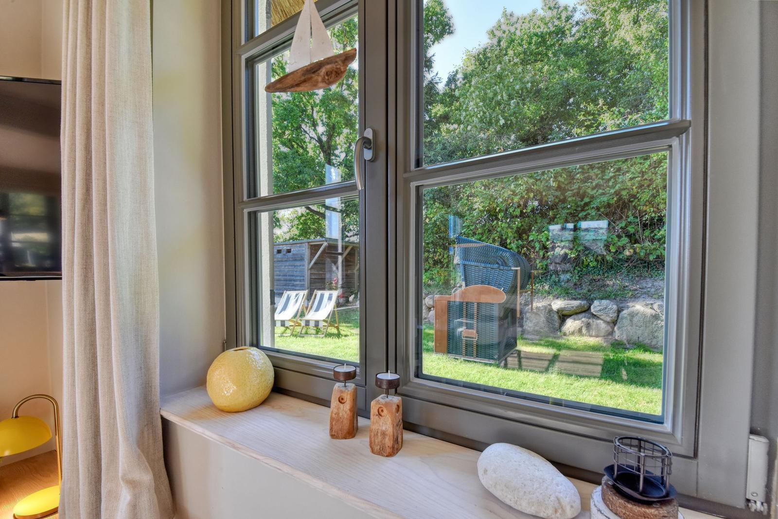 Fensterblick auf grünen Garten mit Liegestühlen und Steinmauer.