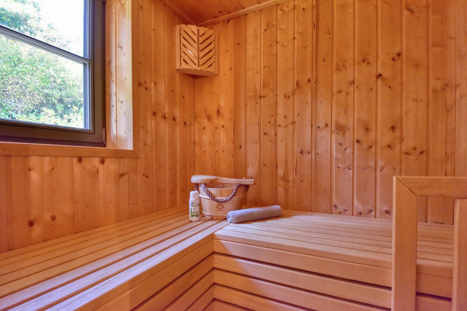 Sauna mit Holzwand, Sitzbank, Eimer und Fenster zur Aussicht.