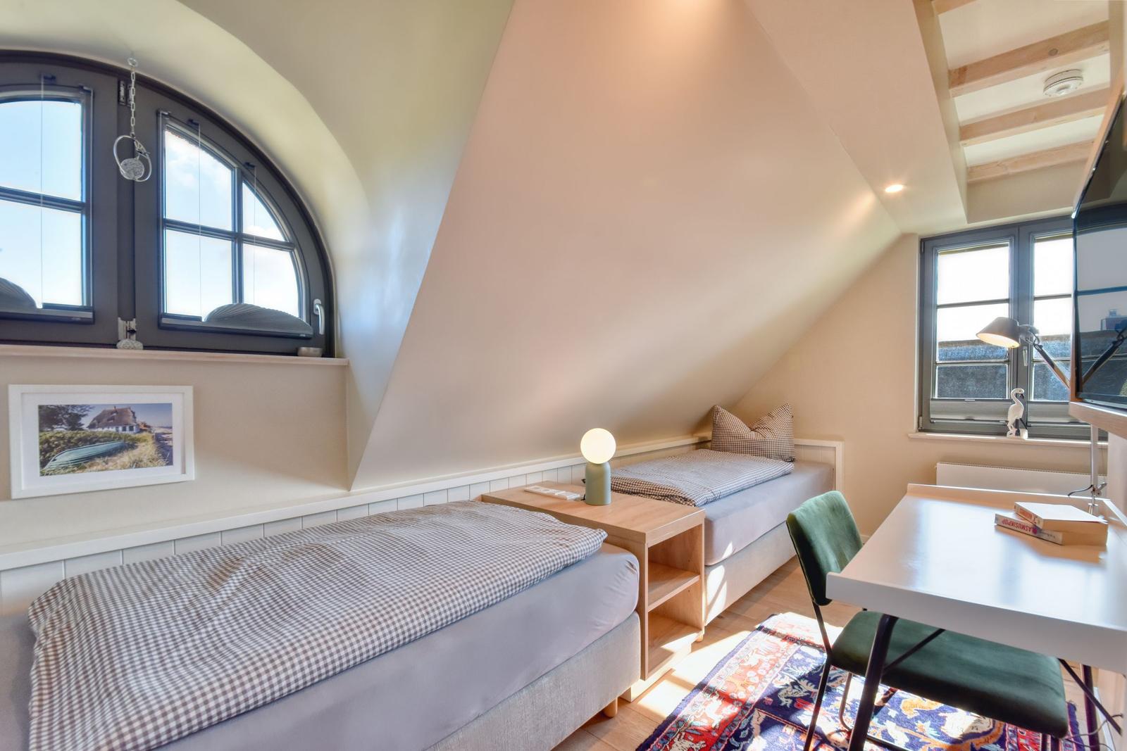 Zimmer mit zwei Betten, Schreibtisch und Fenstern unter schrägem Dach