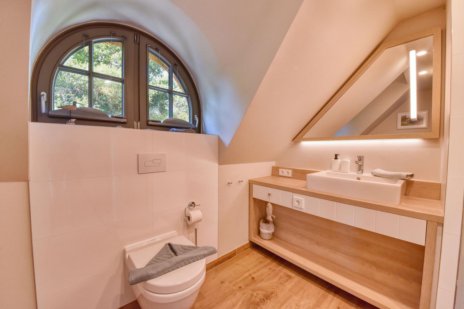 Badezimmer mit Dusche, Waschbecken und Toilette unter einem Dachfenster.