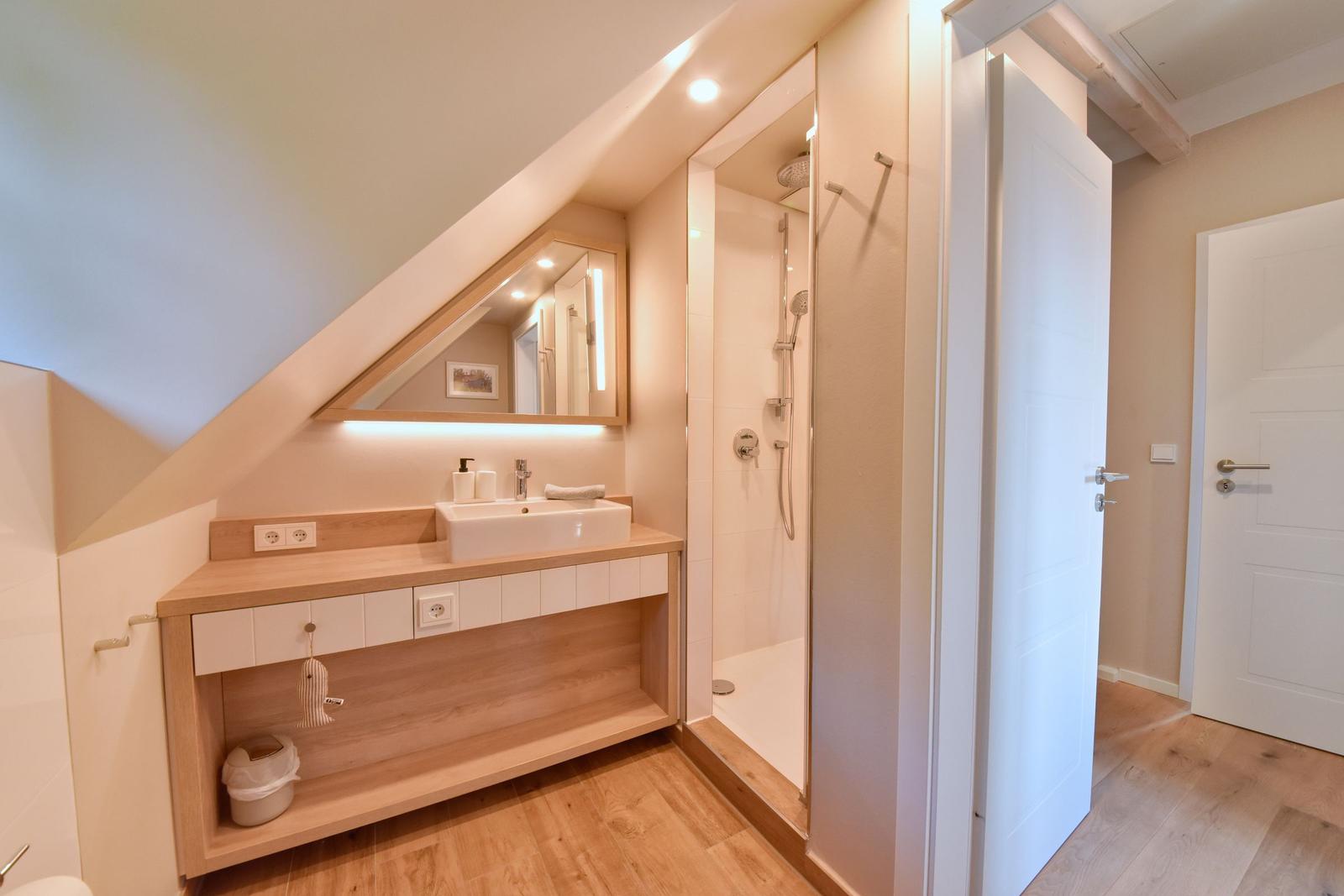 Badezimmer mit Dusche, Waschbecken und Spiegel unter Dachschräge.