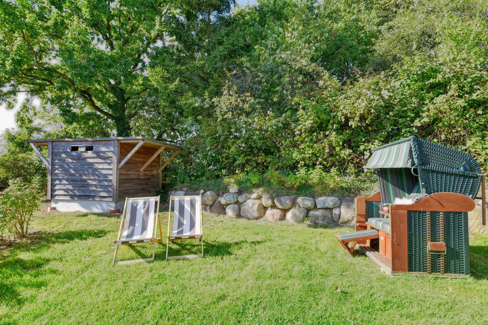 Garten mit Liegestühlen, Strandkorb und Holzschuppen unter Bäumen.