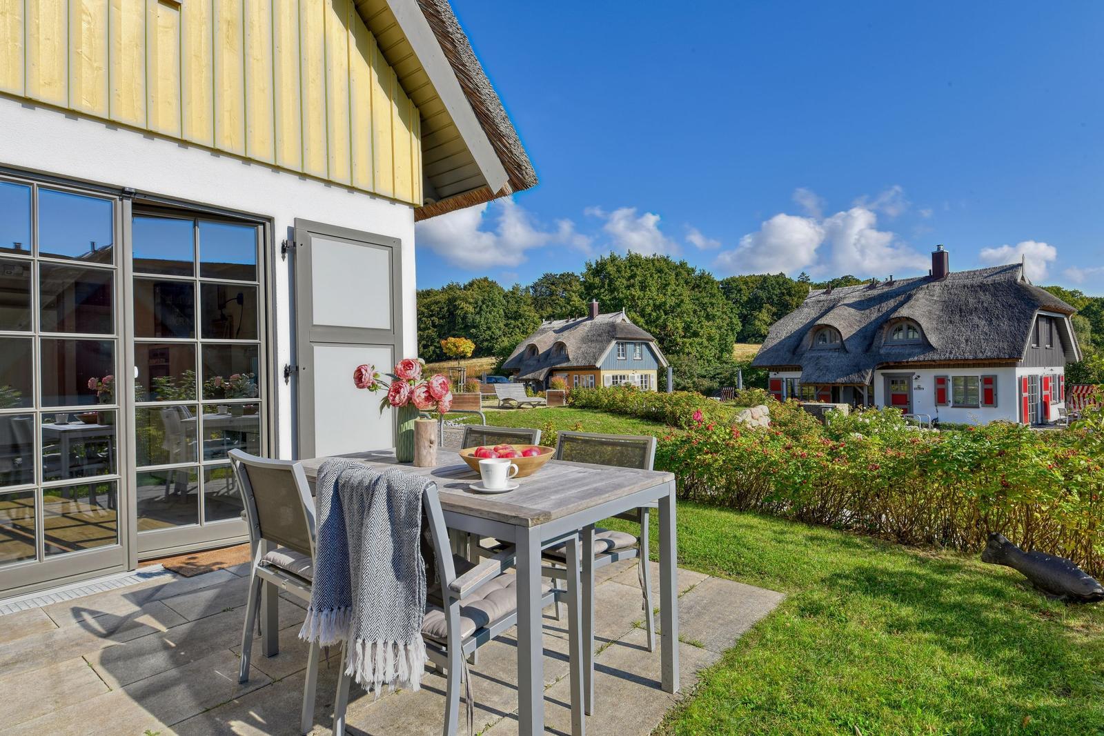 Terrasse mit Tisch und Stühlen. Im Hintergrund sind Häuser mit Strohdächern zu sehen.