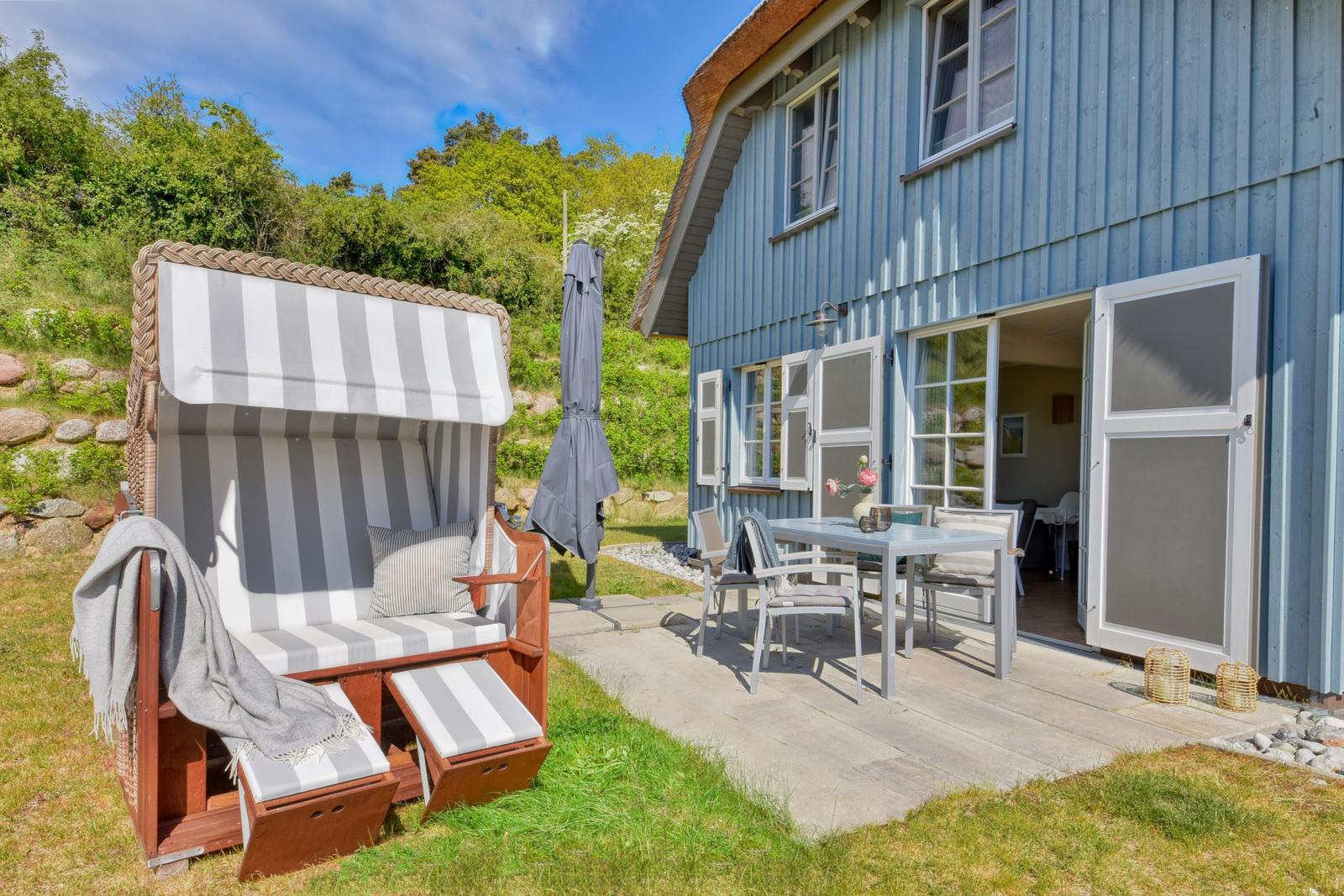 Blue wooden house with terrace, beach chair, and outdoor dining table.