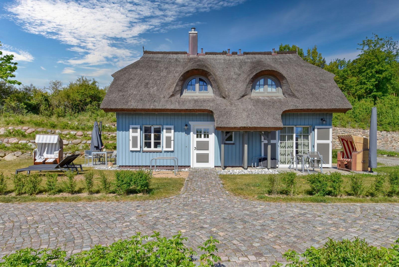 Blue house with thatched roof and garden area with sun loungers.