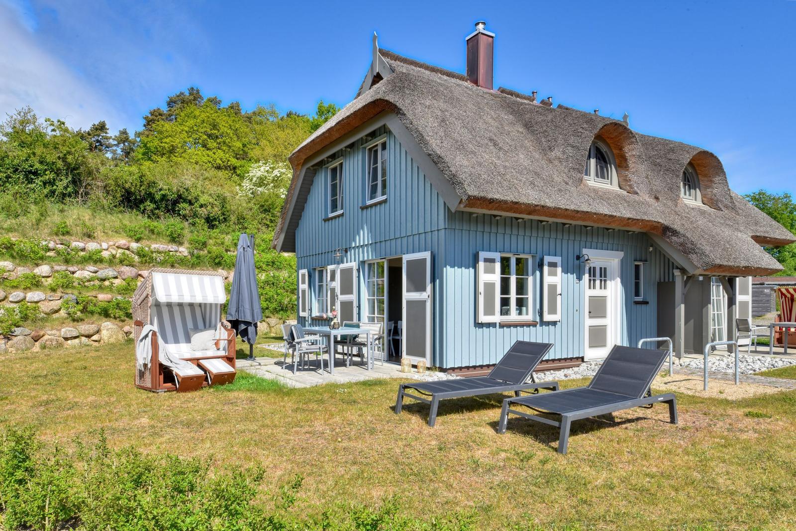 Blue house with thatched roof and garden furniture. Terrace with table and chairs.