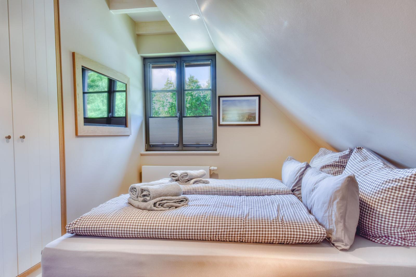 Bedroom with sloped ceiling, bed with checkered bedding, and window with view of trees.