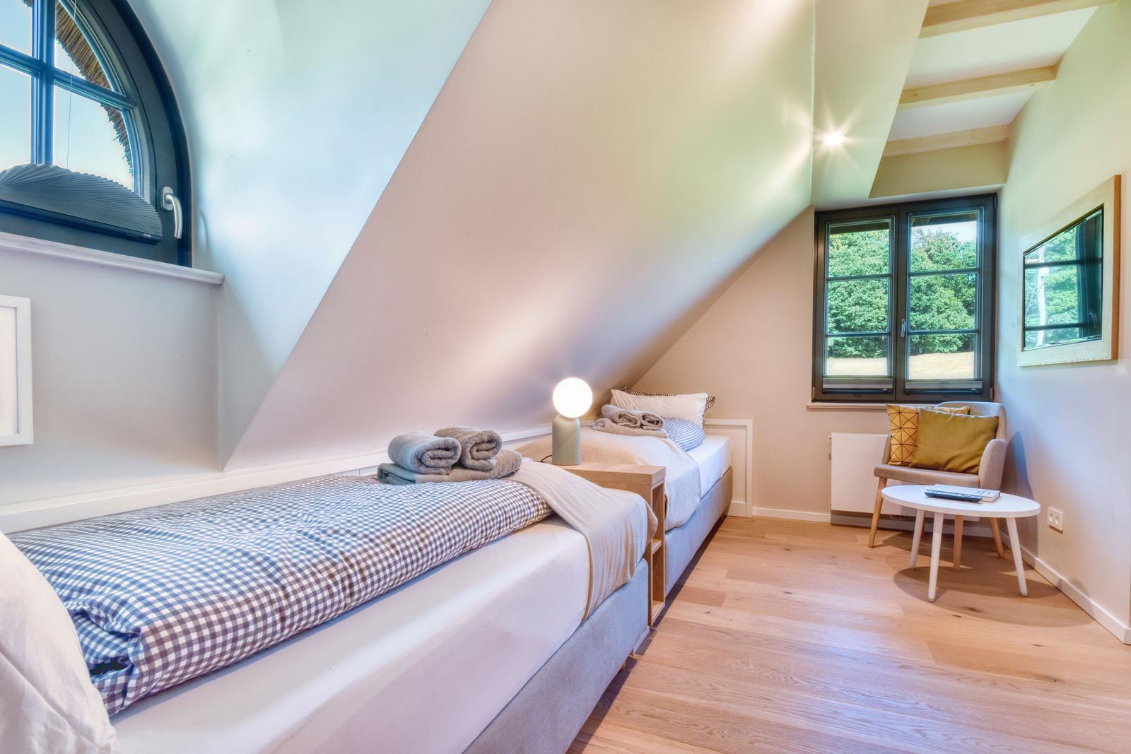 Two beds under sloped ceilings with windows and wooden floor.