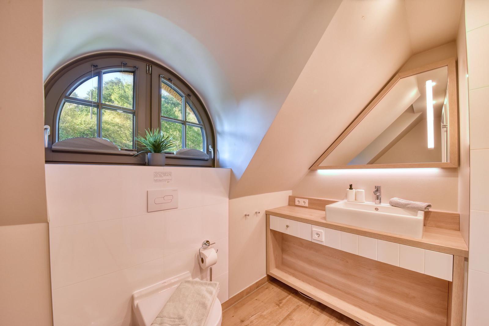 Bathroom with wooden vanity, mirror, and arched window overlooking greenery.