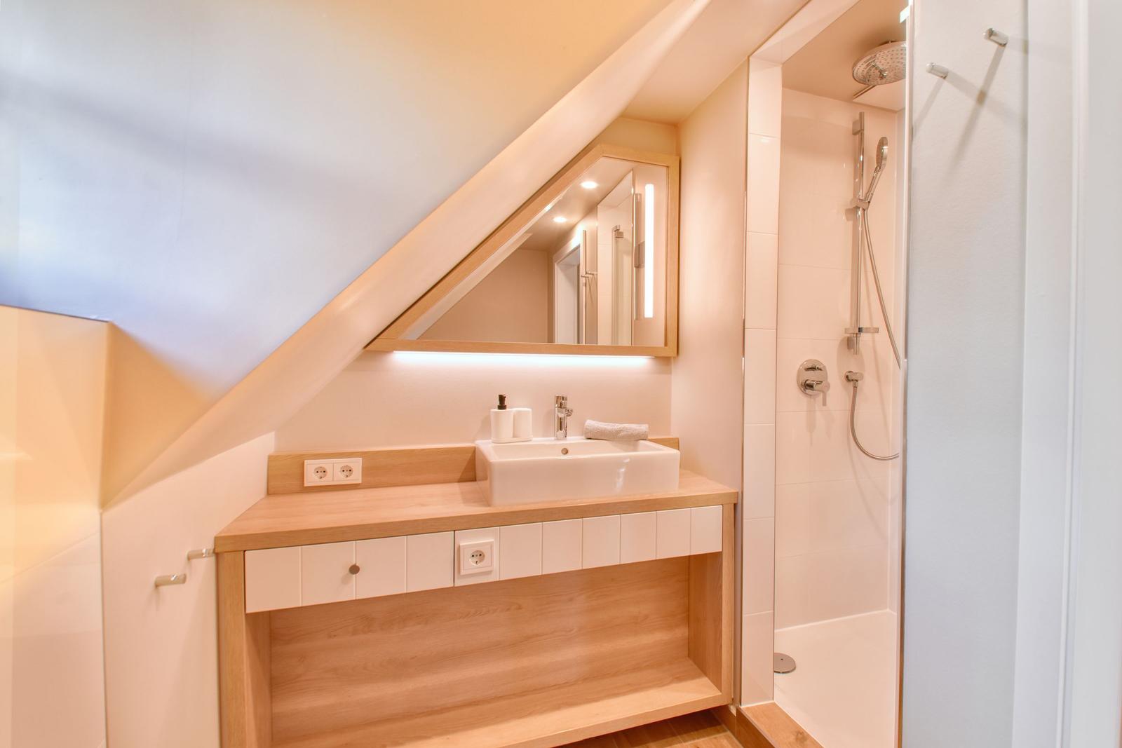 Bathroom with shower, sink, and mirror under sloped ceiling.