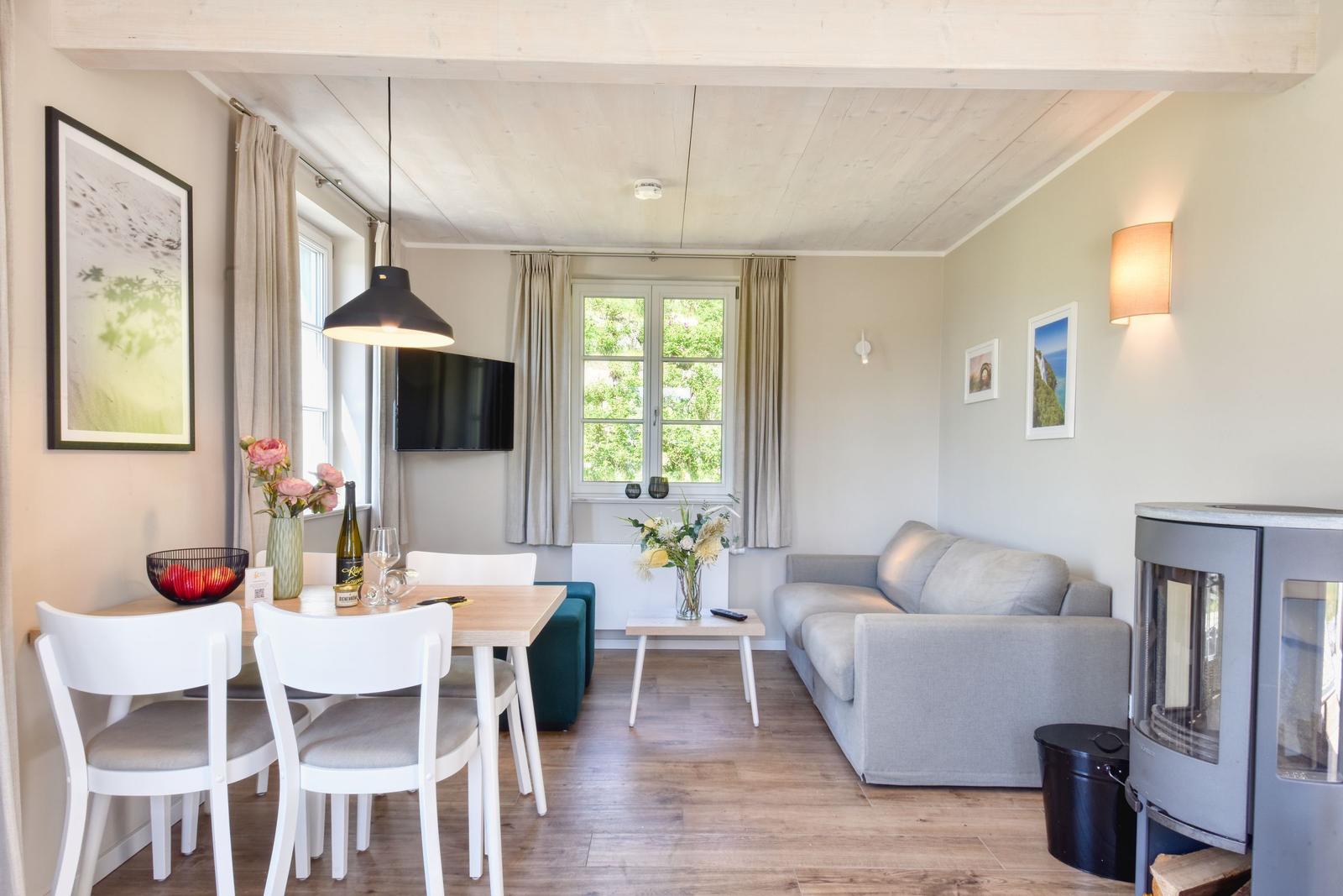 Living and dining area with sofa, dining table, and windows. Wooden floor and ceiling beams.
