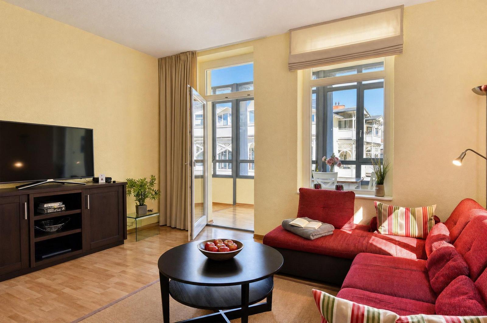 Wohnzimmer mit rotem Sofa, Fernseher und Blick auf Balkon.