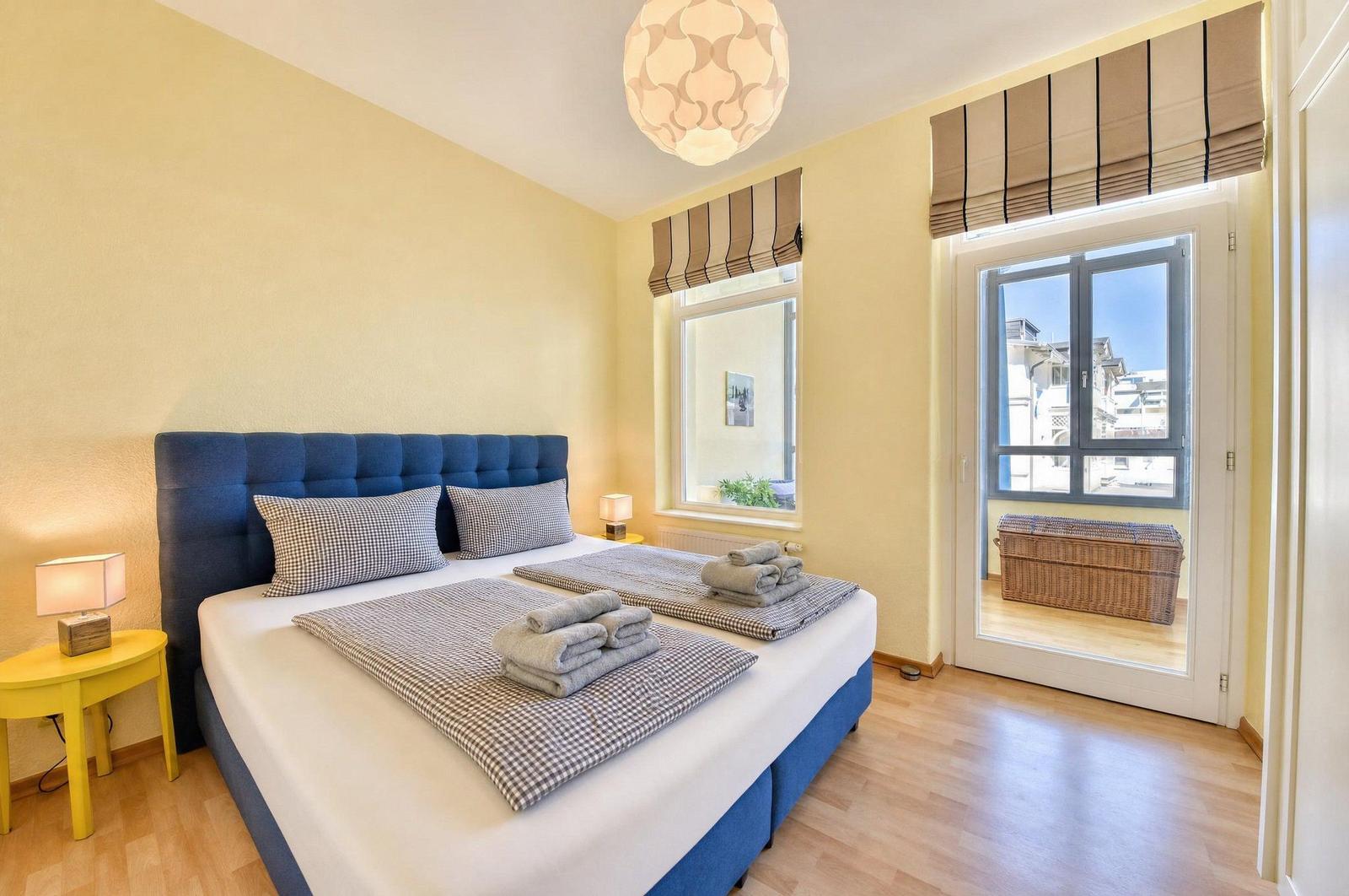 Schlafzimmer mit Doppelbett, Fenster und Tür zum Balkon. Holzboden und gelbe Wände.