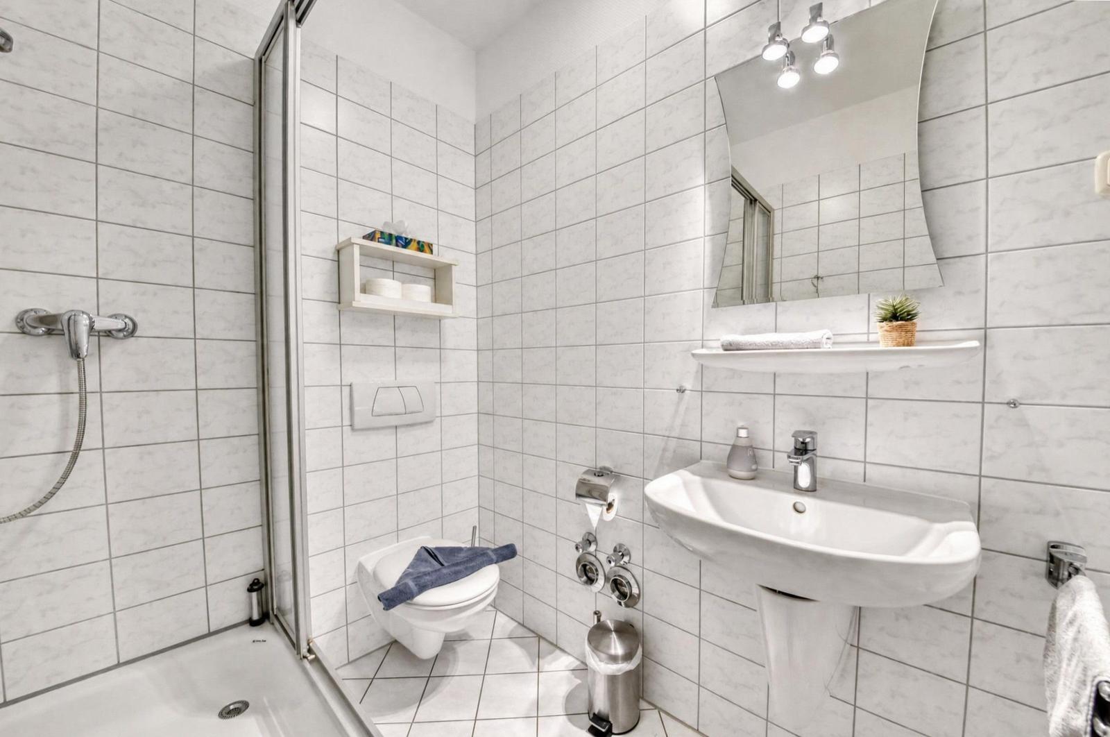 Badezimmer mit Dusche, WC und Waschbecken. Weiße Fliesen und Spiegelschrank.