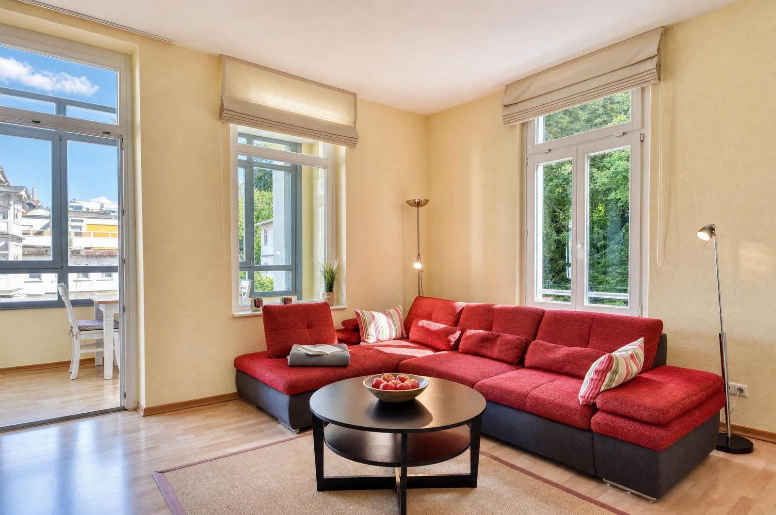 Ein Wohnzimmer mit rotem Sofa, runden Tisch und großen Fenstern.