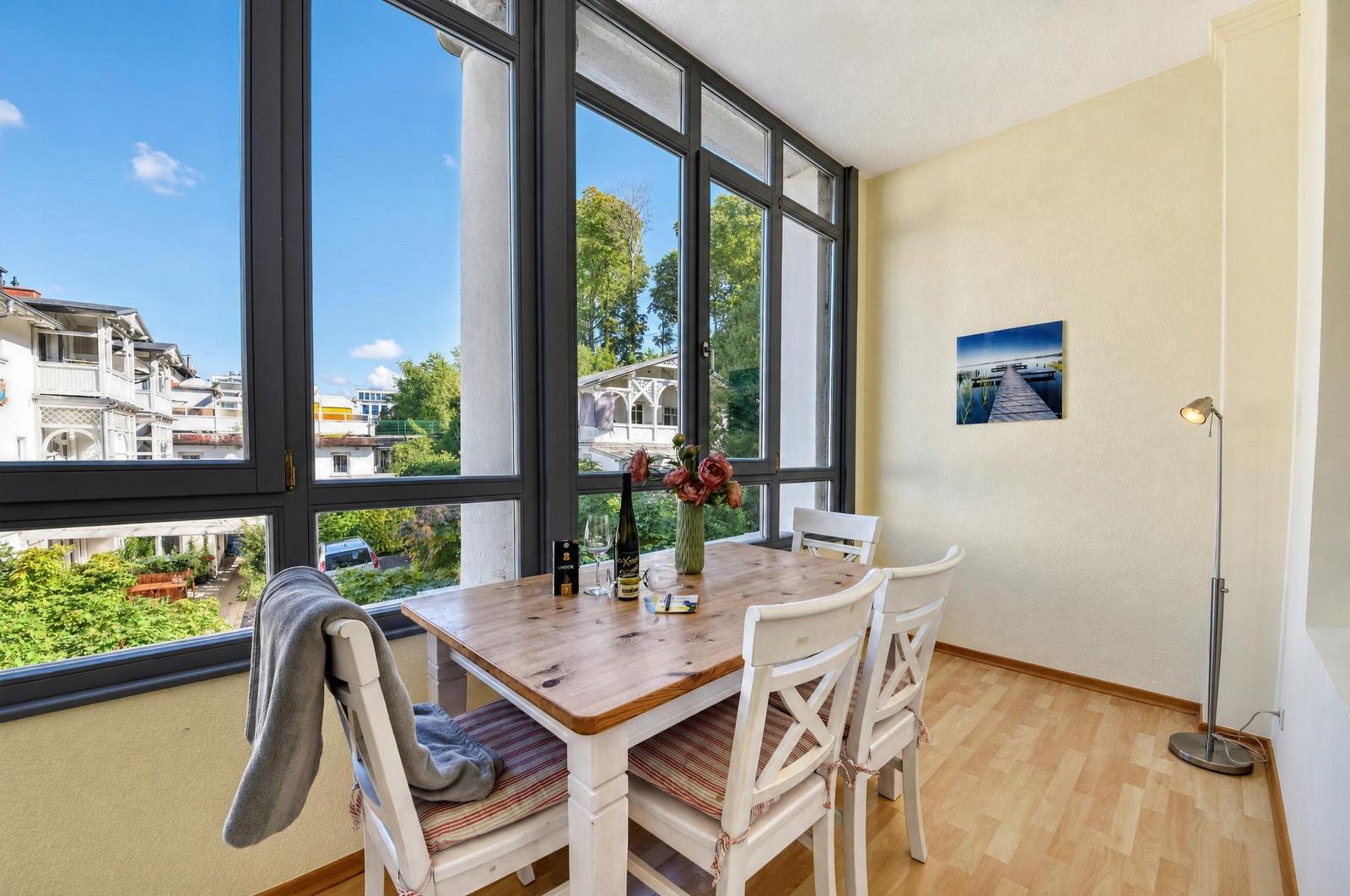 Esszimmer mit Holztisch, weißen Stühlen und großem Fensterblick auf Grün und Gebäude.