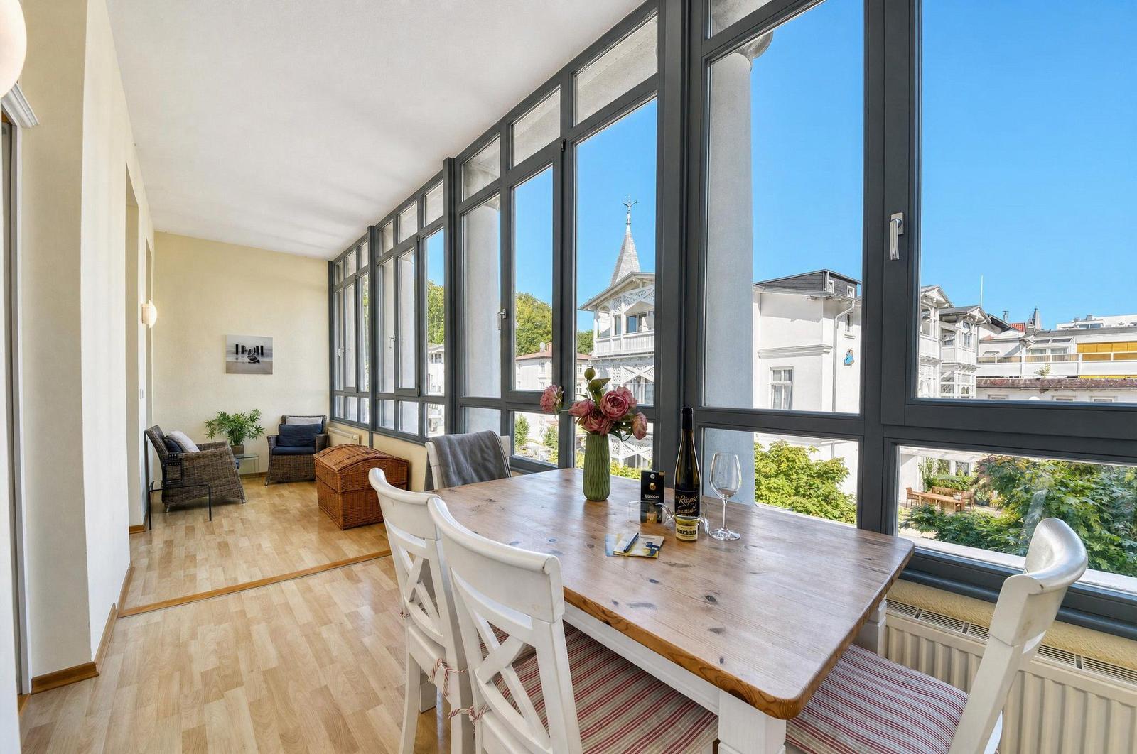 Essbereich mit Tisch und Stühlen, großes Fenster mit Blick auf Gebäude und Bäume.