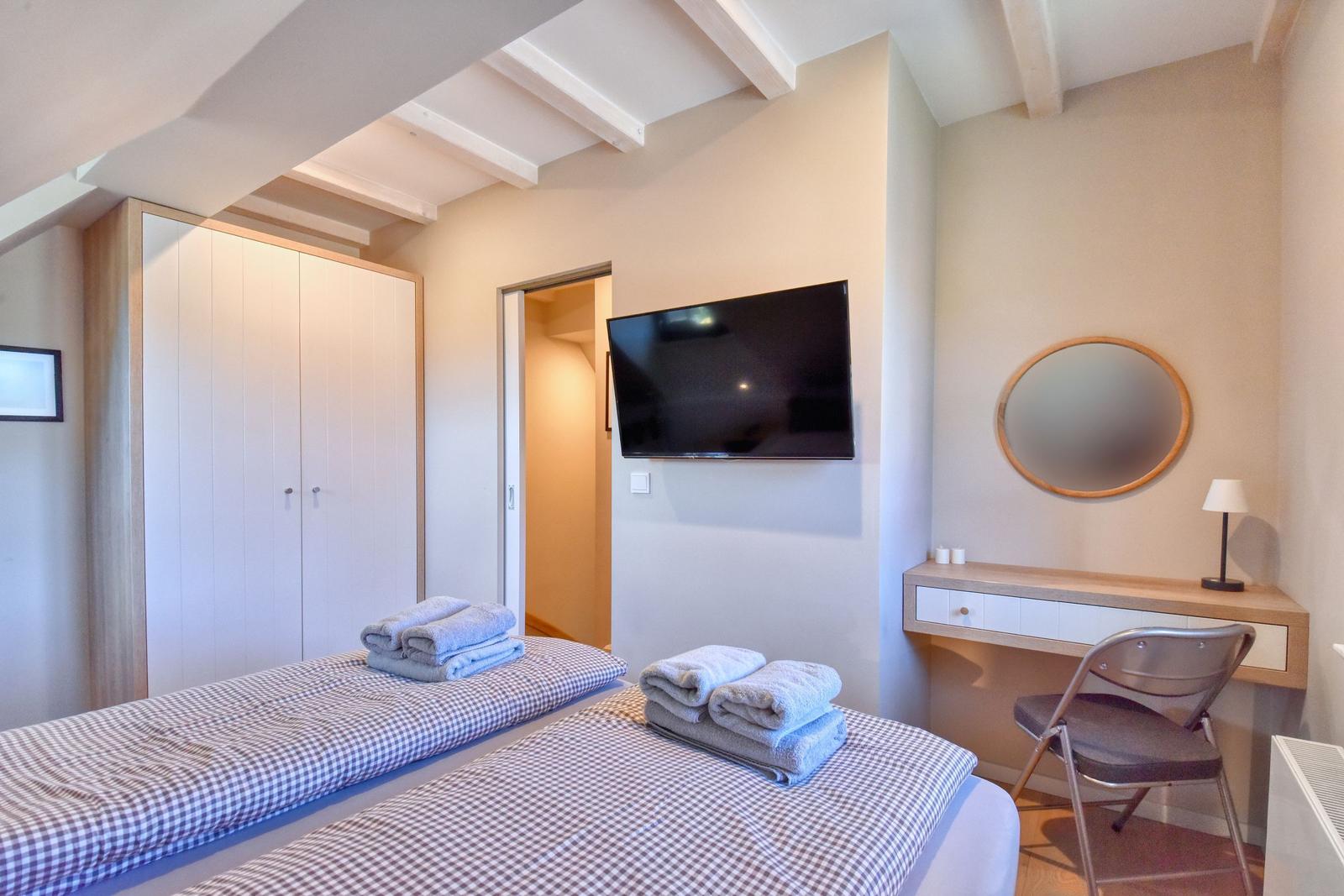 Zimmer mit Doppelbett, Kleiderschrank, Fernseher und Schreibtisch mit Spiegel.