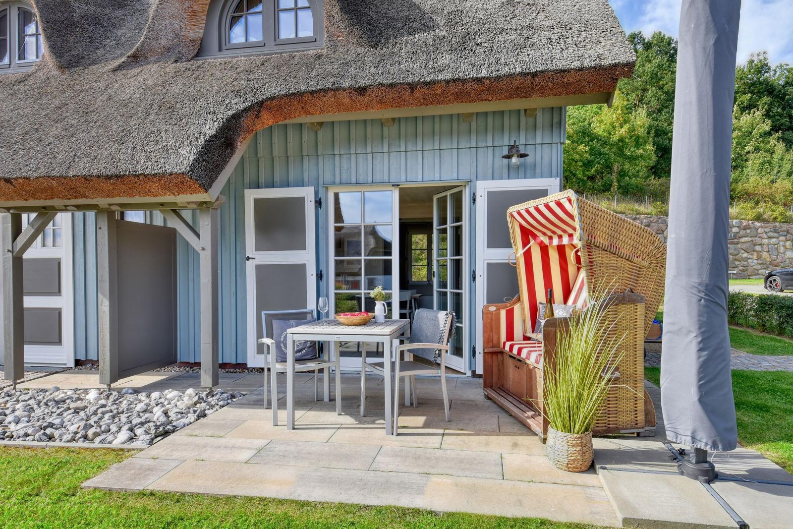 Terrasse mit Tisch, Stühlen und Strandkorb vor einem Haus mit Strohdach.