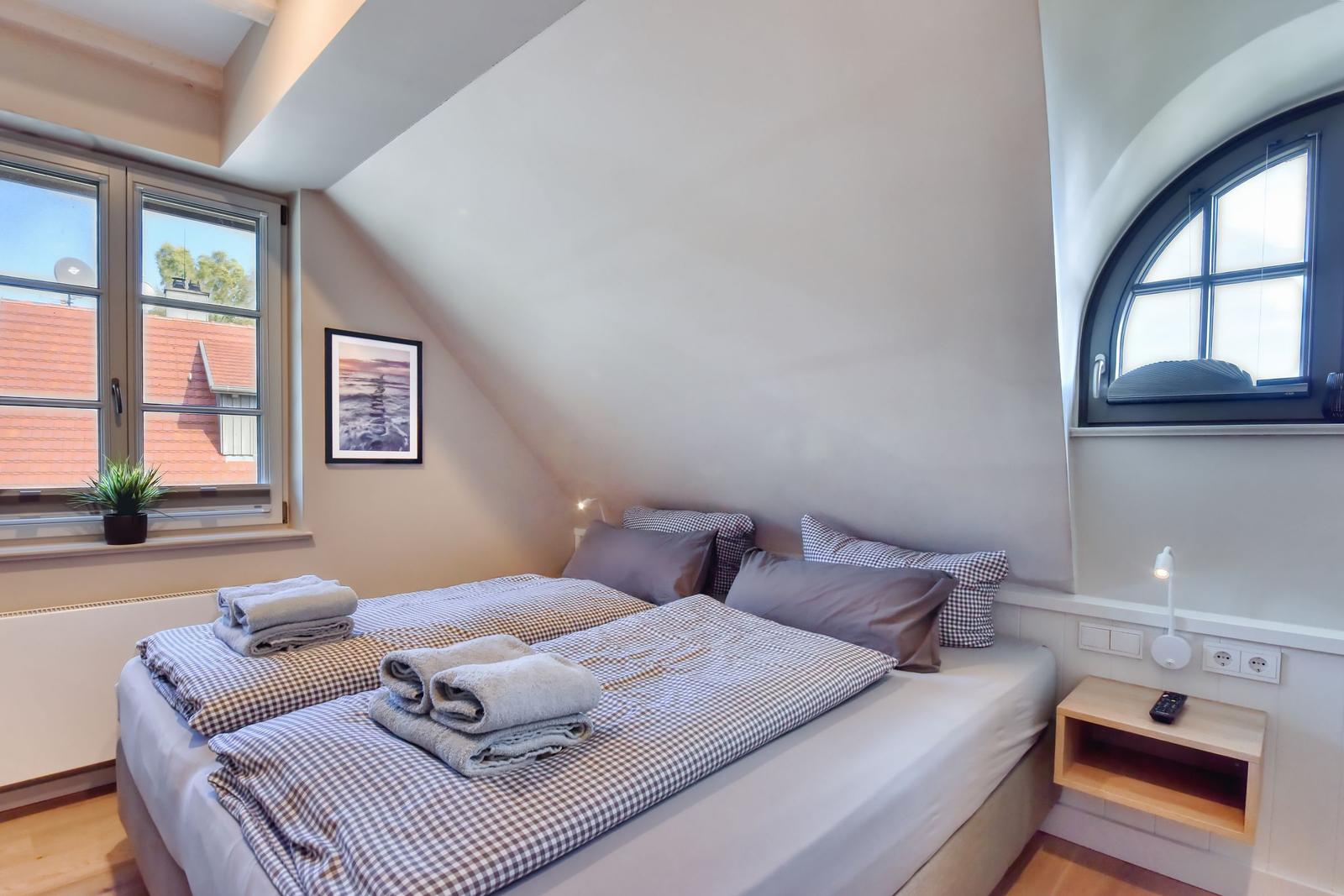 Schlafzimmer mit Doppelbett, Fenster und Nachttisch.