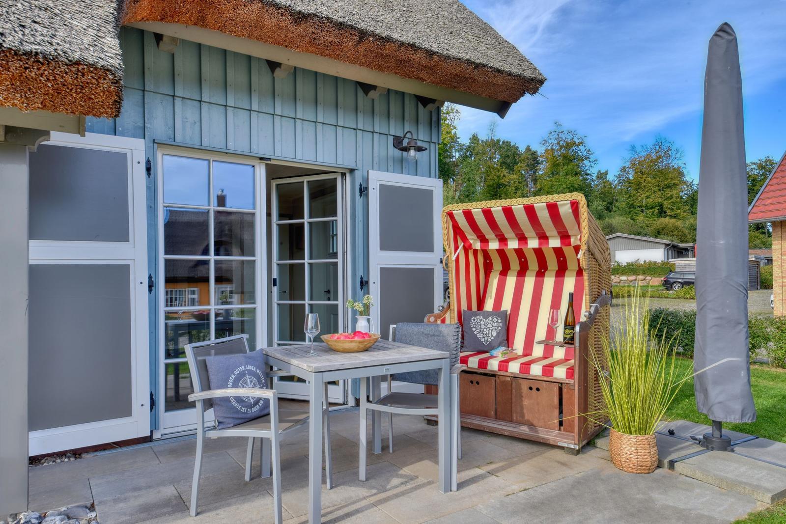 Terrasse mit Esstisch, Stühlen und Strandkorb unter Dach