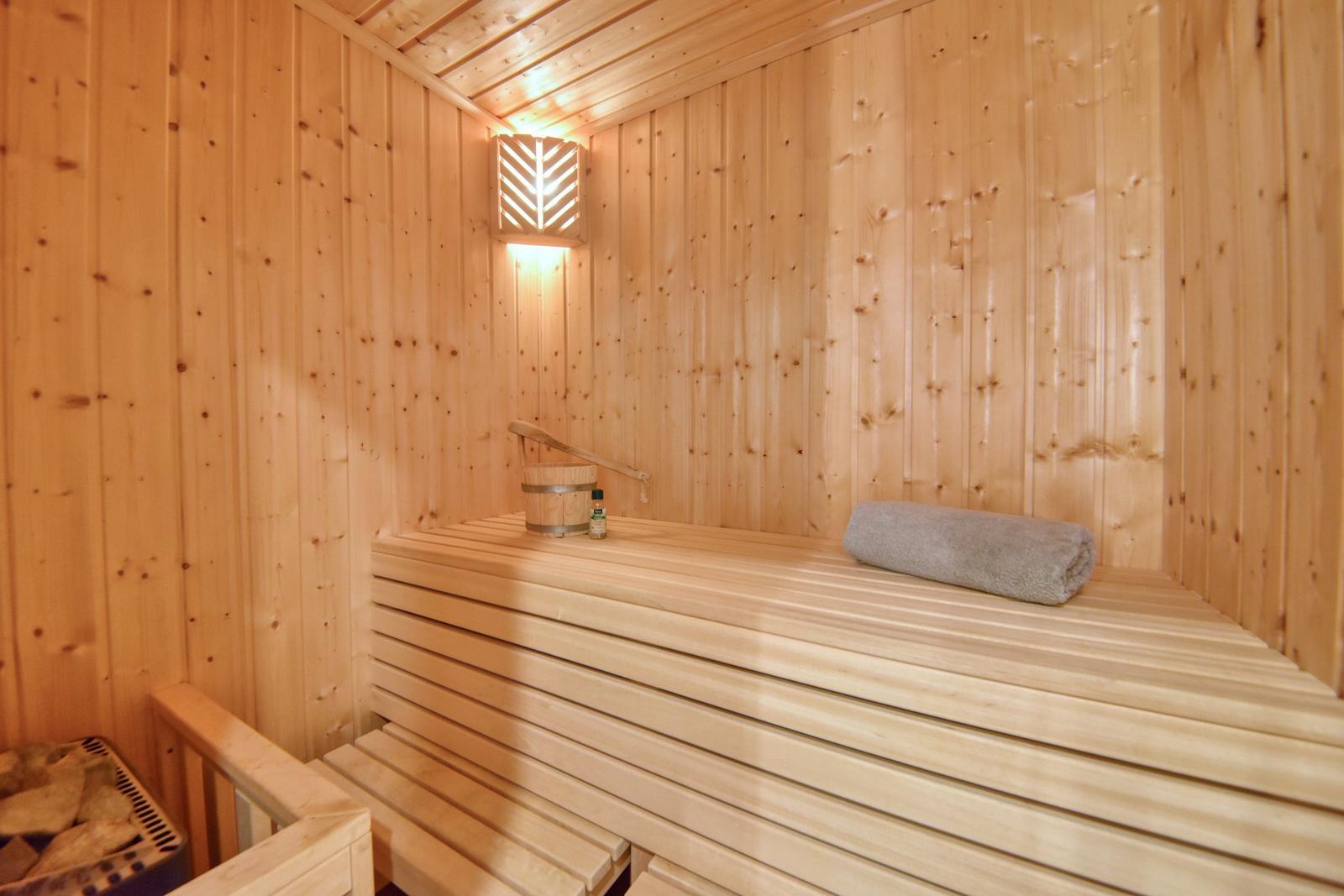 Sauna mit Holzbank, gefalteter Handtuch und Wasserkanister.