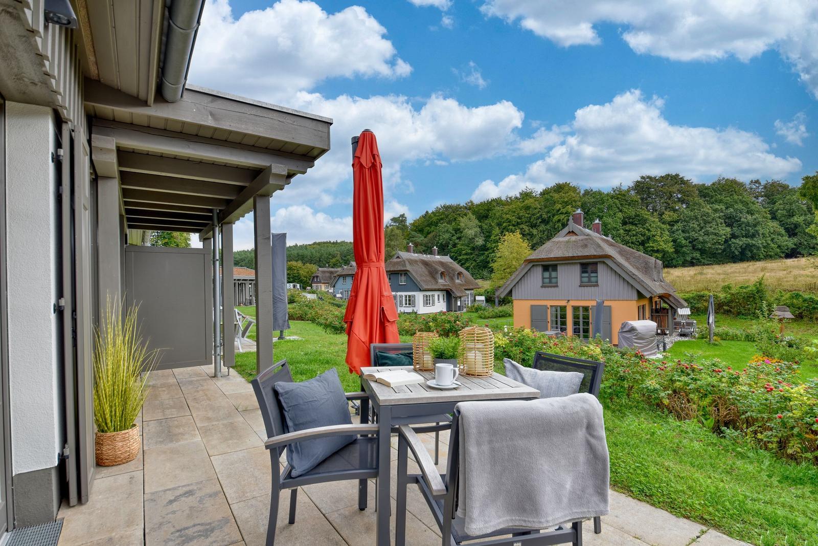 Terrasse mit Tisch, Stühlen und rotem Sonnenschirm. Blick auf Garten und traditionelle Häuser.