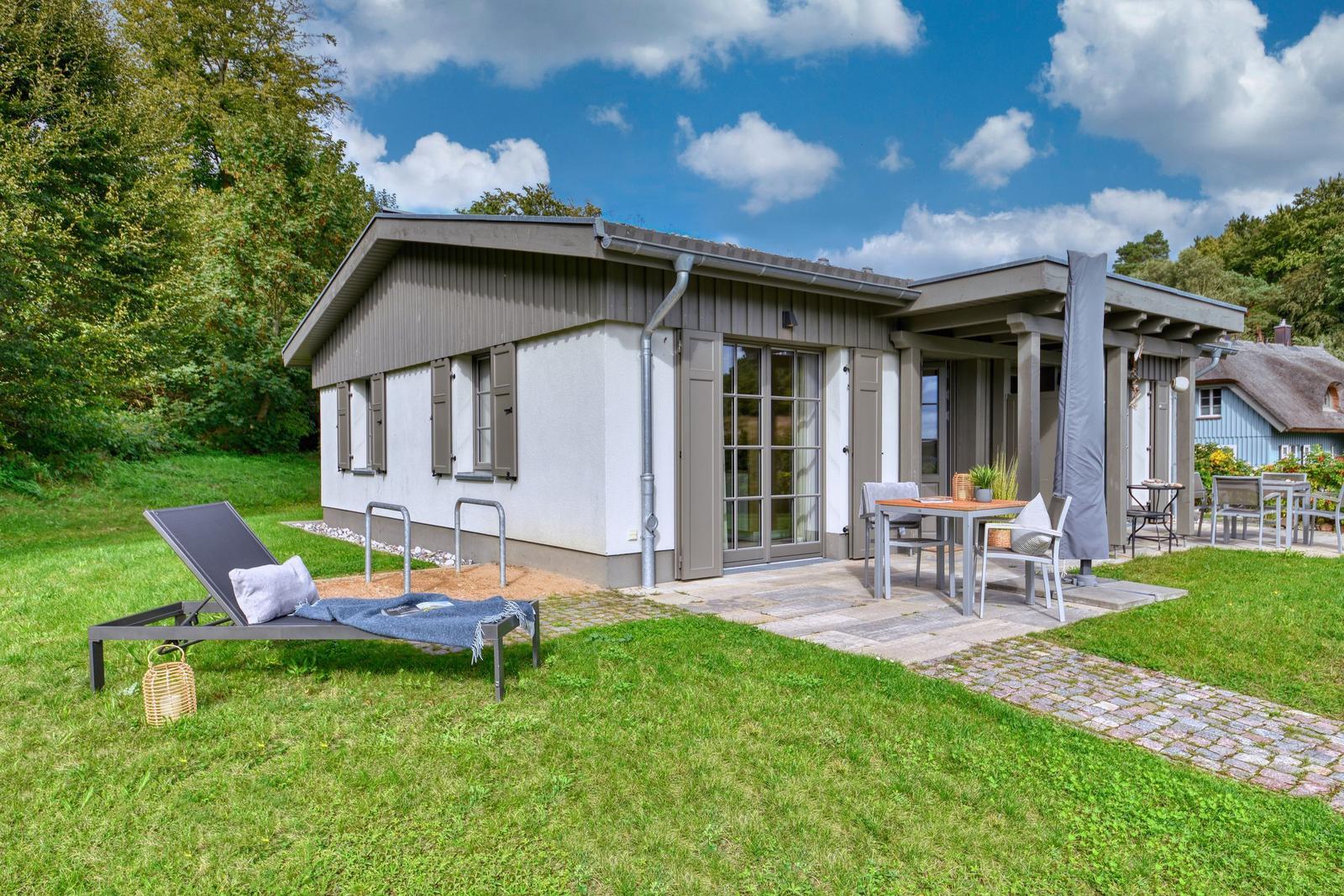 Moderne Villa mit Terrasse, Gartenliege und Grillplatz. Umgeben von Grün und Bäumen.