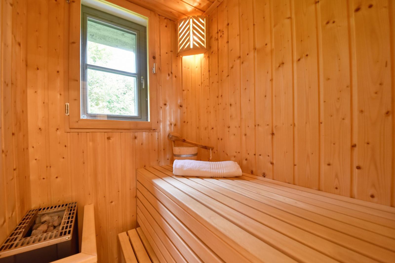 Holzsauna mit Fenster, Bank und Dampfsteinen. Ein weißes Handtuch liegt auf der Bank.