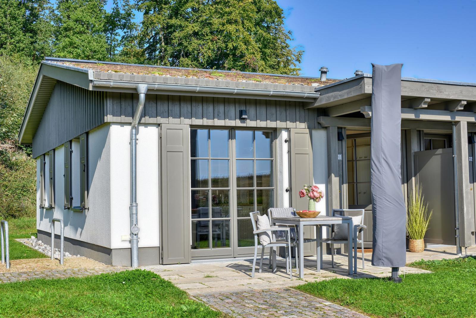 Moderne Ferienwohnung mit Terrasse, Gartentisch und Pflanzen. Dach mit Grünfläche.
