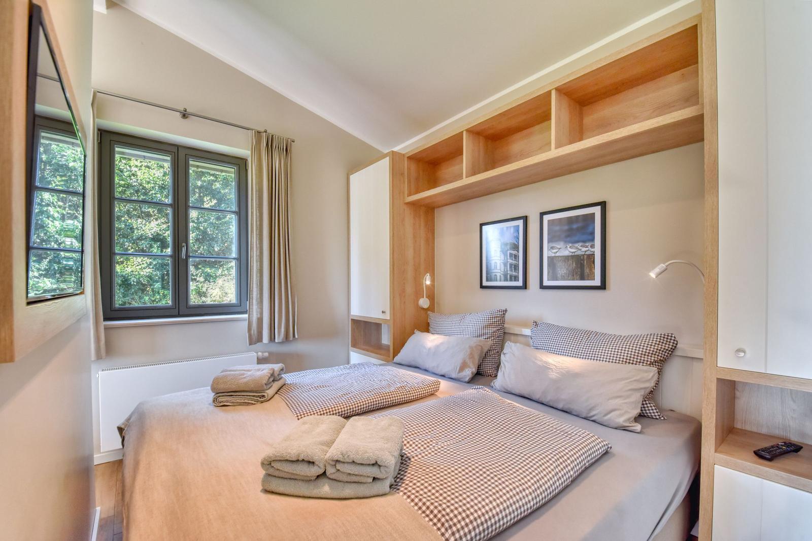 Schlafzimmer mit Bett, Fenster und integrierten Schränken. Auf dem Bett liegen Handtücher.