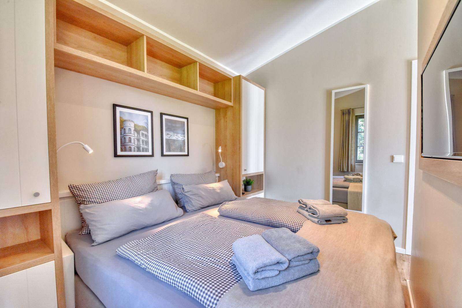 Schlafzimmer mit Doppelbett, Holzmöbel und Spiegel. Handtuch und Bettwäsche sind bereit.