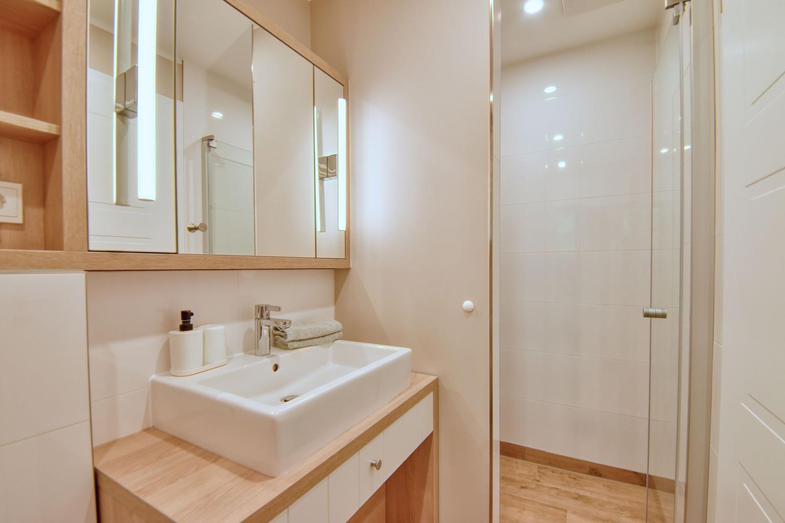 Bad mit Waschbecken, Spiegelschrank und Dusche mit Glaswand.