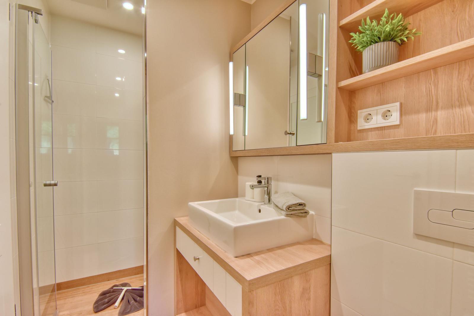 Badezimmer mit Dusche, Waschbecken und Spiegelschrank mit beleuchteten Spiegeln.