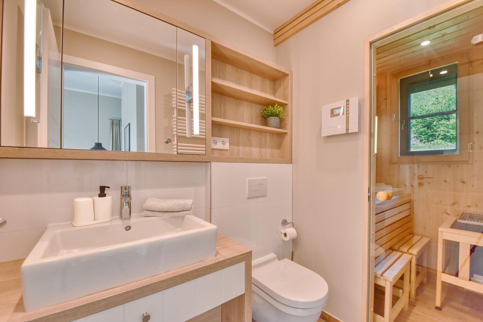Bad mit Waschbecken, Spiegel und Sauna im Hintergrund.