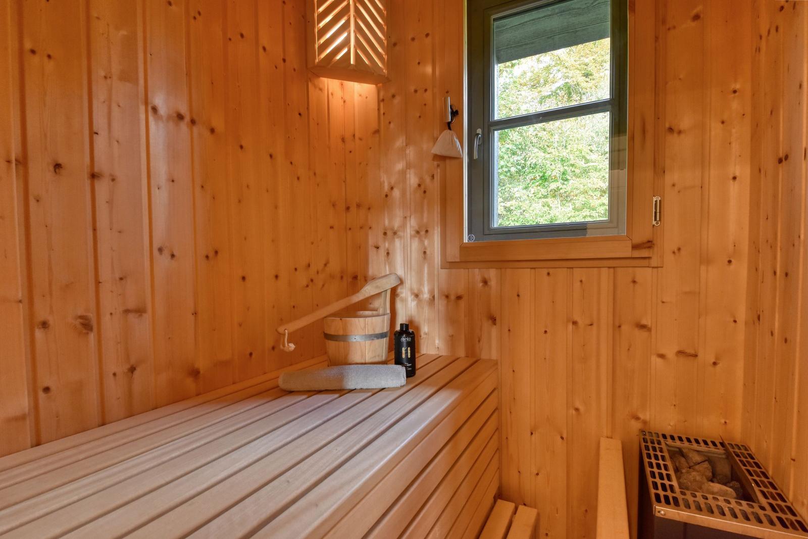 Sauna mit Holzwand, Sitzbank, Eimer und Fenster zur Natur.