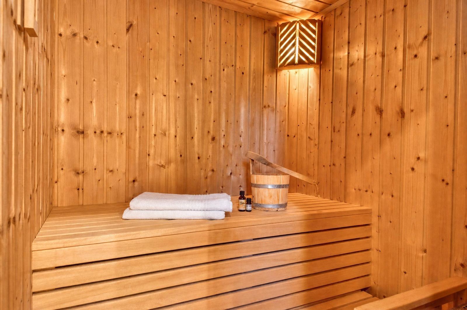 Sauna mit Holzwand, Holzbank, Handtuch, Eimer und Öle.
