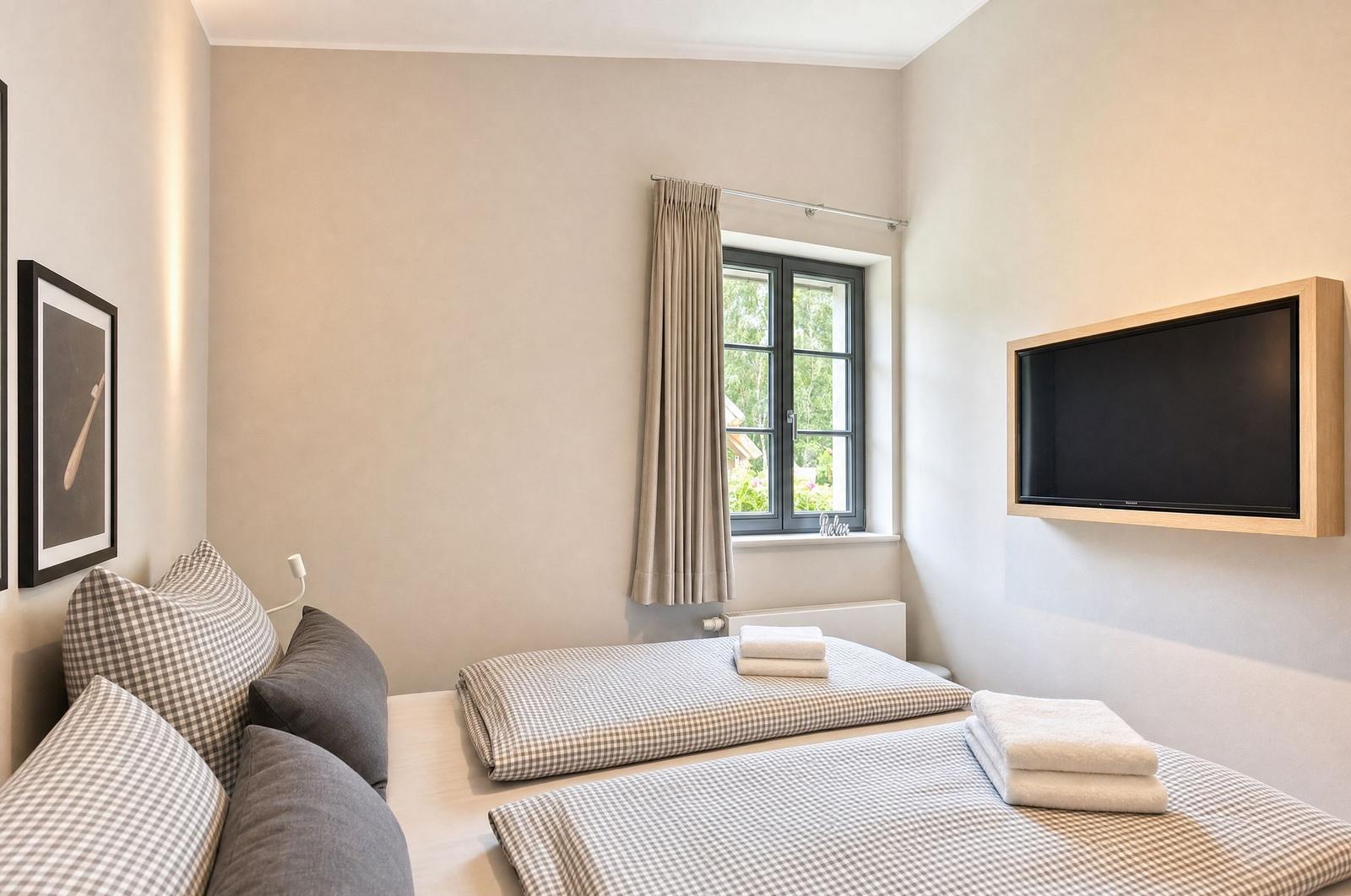 Zimmer mit zwei Betten, Fenster und Wandfernseher.