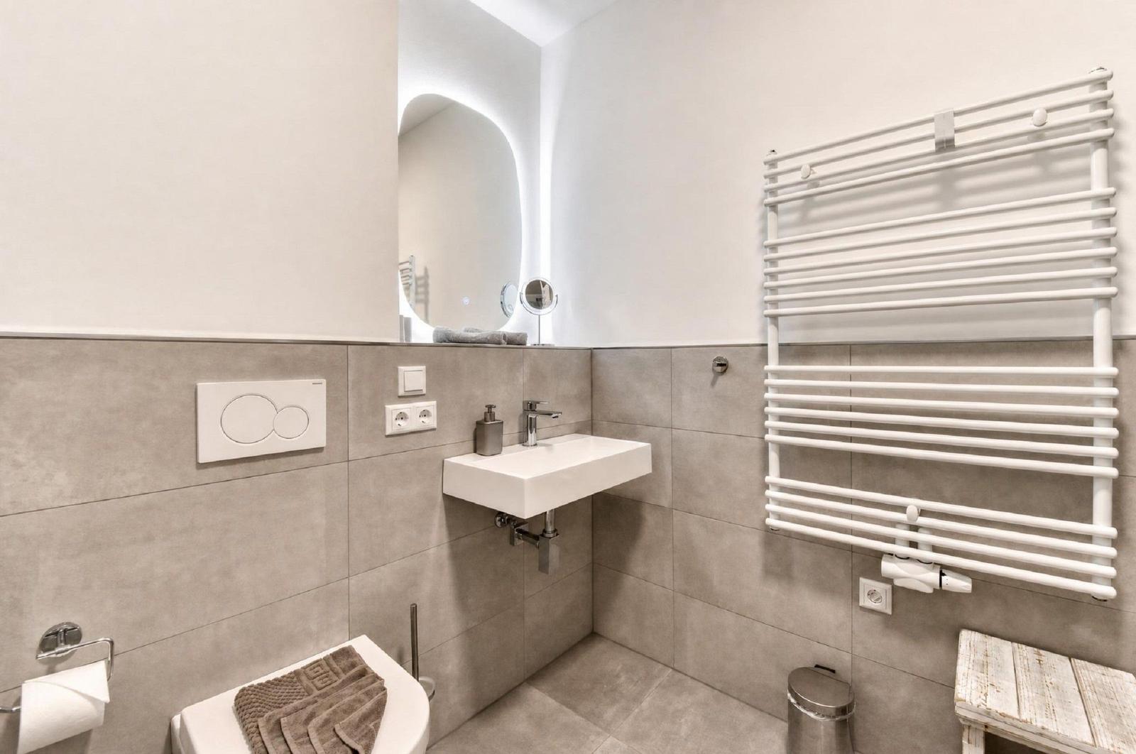 Badezimmer mit Waschbecken, Spiegel, Heizkörper und Toilette.