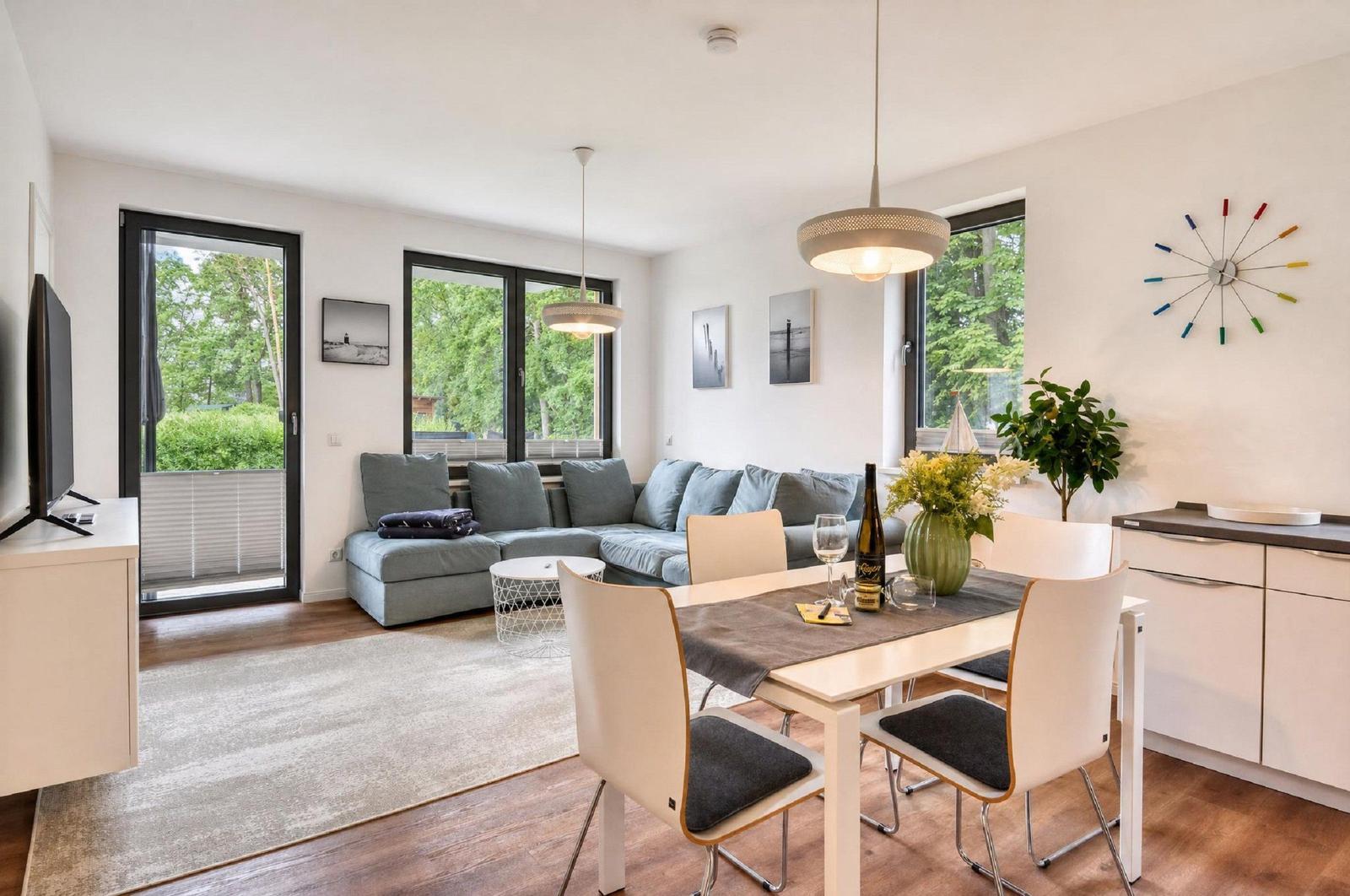 Wohn- und Essbereich mit Sofa, Tisch und Stühlen. Fenster mit Blick auf Grün.